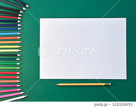 A blank sheet of paper is placed on a green surface. Surrounding it are various colored pencils, A blank sheet of paper is placed on a green surface. Surrounding it are various colored pencils, 128326055
