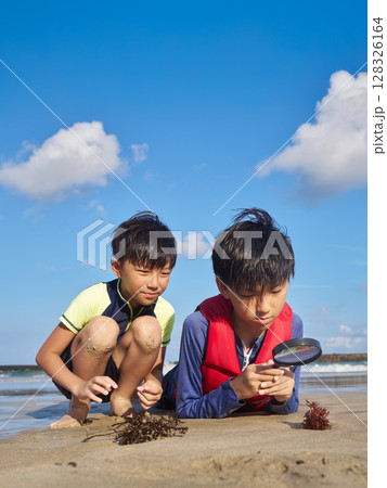 夏の砂浜で虫眼鏡を使って自然観察をする小学生 夏の砂浜で虫眼鏡を使って自然観察をする小学生 128326164