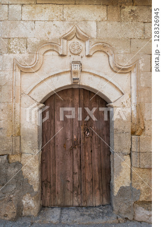 Weathered wooden door with ornate stone archway and star carving, traditional European architecture Weathered wooden door with ornate stone archway and star carving, traditional European architecture 128326945