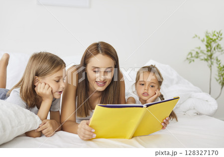 Happy family reading in bed, parents and cute small kids laughing lying together, children bonding Happy family reading in bed, parents and cute small kids laughing lying together, children bonding 128327170