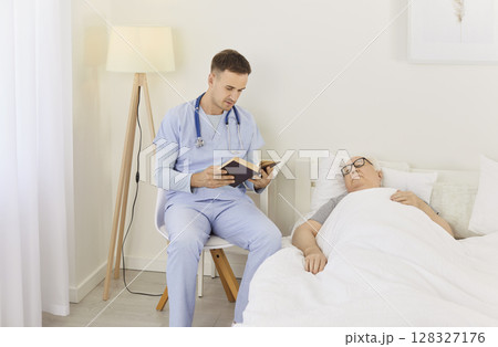 In bright hospital room, compassionate doctor reads book while sitting next to his elderly patient. In bright hospital room, compassionate doctor reads book while sitting next to his elderly patient. 128327176