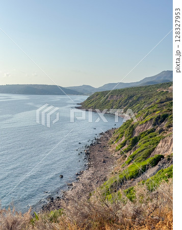 Stunning view of a rugged coastline with green cliffs and the expansive sea. The contrasting textures of rock and lush vegetation form a captivating natural landscape. 128327953