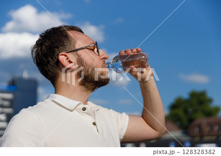 Man Enjoying Refreshing Water from a Bottle Under Clear Blue Sky with Fluffy Clouds on a Bright Day Perfect for Hydration and Outdoor Activities in Summer Man Enjoying Refreshing Water from a Bottle Under Clear Blue Sky with Fluffy Clouds on a Bright Day Perfect for Hydration and Outdoor Activities in Summer 128328382