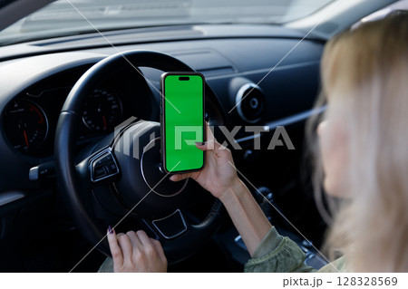 A Close-Up in a Car Interior Featuring a Hand Holding a Smartphone with a Green Screen, Ideal for Customizable Content Creation and Digital Applications 128328569