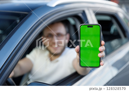 A Smiling Driver Displaying a Green Screen Smartphone from His Car Window, Representing Technology and Connectivity in Modern Transportation 128328570