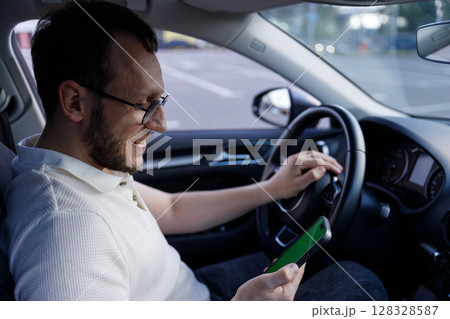 A Man Enjoying His Time in the Car While Using His Smartphone, Capturing a Moment of Relaxation and Engagement with Mobile Technology on a Sunny Day A Man Enjoying His Time in the Car While Using His Smartphone, Capturing a Moment of Relaxation and Engagement with Mobile Technology on a Sunny Day 128328587