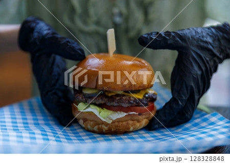 Deliciously Juicy Burger with Toppings, Served on a Checkered Paper, Perfect for Food Lovers and Fast Food Enthusiasts, Ready to be Enjoyed in a Cozy Setting. Deliciously Juicy Burger with Toppings, Served on a Checkered Paper, Perfect for Food Lovers and Fast Food Enthusiasts, Ready to be Enjoyed in a Cozy Setting. 128328848