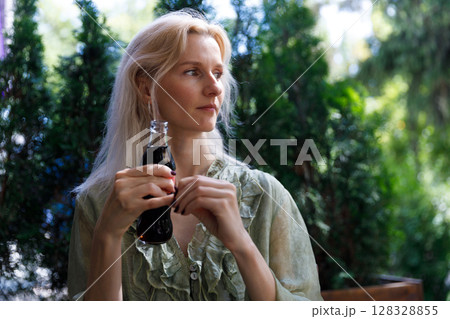 Contemplative Woman Enjoying a Beverage in a Lush Outdoor Setting, Exuding a Sense of Peace and Calm Amongst Nature's Greenery 128328855