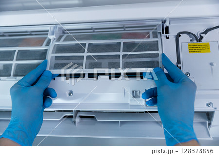 A Close-up View of Hands in Blue Gloves Carefully Removing the Filter from an Air Conditioning Unit for Maintenance and Cleaning to Ensure Efficient Performance and Air Quality A Close-up View of Hands in Blue Gloves Carefully Removing the Filter from an Air Conditioning Unit for Maintenance and Cleaning to Ensure Efficient Performance and Air Quality 128328856