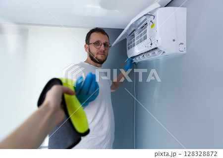 A Professional Male in Protective Gloves Working on an Air Conditioning Unit, Engaged in Maintenance at Home, Showcasing Cleanliness and Expertise for Comfortable Living Environments 128328872
