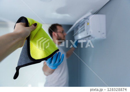 A Man Cleaning an Air Conditioner with a Cloth: The Importance of Maintenance for Optimal Air Quality and Efficiency in Indoor Spaces A Man Cleaning an Air Conditioner with a Cloth: The Importance of Maintenance for Optimal Air Quality and Efficiency in Indoor Spaces 128328874