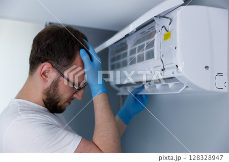 Frustrated technician dealing with air conditioning repair while wearing blue gloves, showing signs of stress and concentration in a modern residential environment 128328947