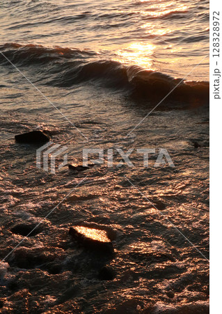 Golden Reflections on Glistening Waves at Sunset Captivating the Serenity of the Ocean with Rocks Submerged in the Glimmering Water under a Vibrant Sky Golden Reflections on Glistening Waves at Sunset Captivating the Serenity of the Ocean with Rocks Submerged in the Glimmering Water under a Vibrant Sky 128328972