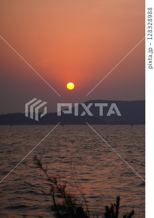 Breathtaking Sunset Over the Calm Waters with a Silhouette of Distant Mountains and Softly Rippling Waves Reflecting Warm Shades of the Setting Sun Breathtaking Sunset Over the Calm Waters with a Silhouette of Distant Mountains and Softly Rippling Waves Reflecting Warm Shades of the Setting Sun 128328988