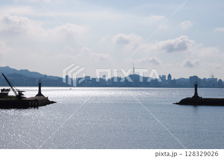 Stunning Coastal View Featuring Lighthouses and City Skyline Under a Bright Sky with Rolling Clouds and Shimmering Water Surface - A Perfect Representation of Urban and Natural Harmony Stunning Coastal View Featuring Lighthouses and City Skyline Under a Bright Sky with Rolling Clouds and Shimmering Water Surface - A Perfect Representation of Urban and Natural Harmony 128329026