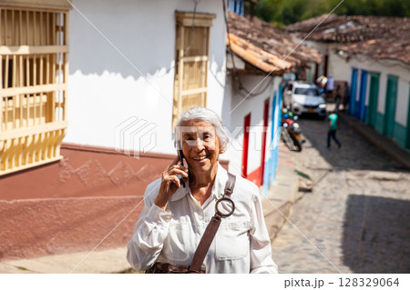 Senior woman using her cellphone ourdoors. Senior woman at the beautiful colonial town of Concepcion located in the department of Antioquia in Colombia. 128329064