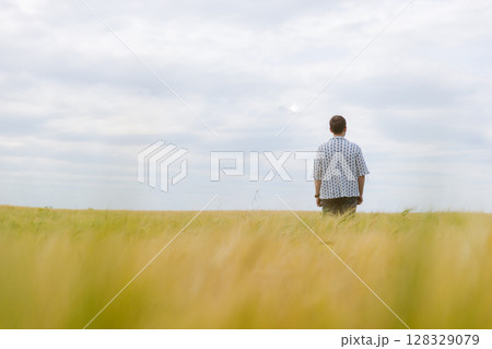 A Contemplative Individual Stands in a Golden Field Under a Vast Sky, Eliciting Thoughts of Nature's Beauty and Personal Reflection Amidst a Calm Atmosphere 128329079