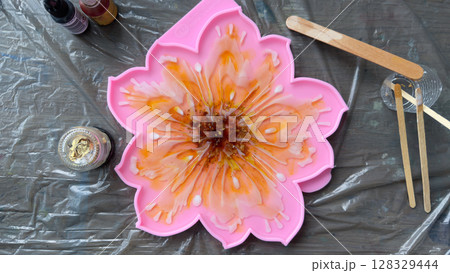 Vibrant Floral Resin Art Creation in a Pink Silicone Mold with Tools and Paints for Crafting Inspiring Artistic Projects at Home or Workshop Settings 128329444