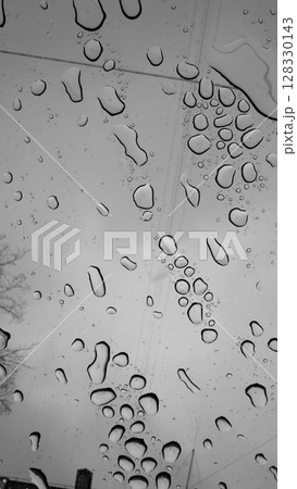 An Atmospheric Black and White Capture of Raindrops on a Window with a Glistening Texture and a Gloomy Sky as the Backdrop Creates a Moody Aesthetic Experience 128330143