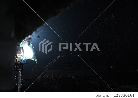 Nighttime Scene with Dramatic Lighting and Falling Snowflakes Captured in a Dark Environment Featuring a Bright Spotlight 128330161