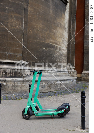A Bright Mint Green Electric Scooter Parked Against a Weathered Stone Wall, Showcasing Urban Mobility in Modern City Infrastructure and Overgrown Nature Beneath the Scooter 128330187