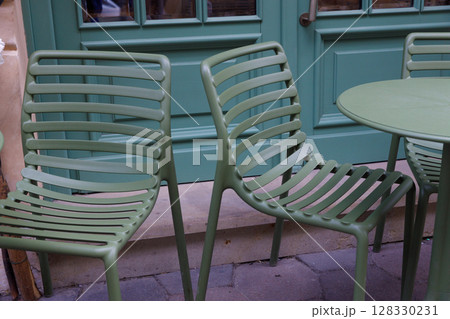 Charming Green Outdoor Furniture: Stylish Slatted Chairs and Round Table Add Elegance to Any Caf Space, Perfect for Relaxing and Enjoying Time Outdoors During Beautiful Weather 128330231