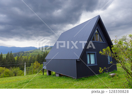 Modern A-Frame House Amidst Lush Greenery and Dramatic Skies with Rolling Hills in the Background, Perfect Representation of Minimalist Architecture in Nature 128330828