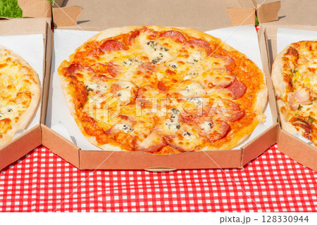 Picnic with pizza. Three different pizzas in a paper bag on a checkered tablecloth 128330944