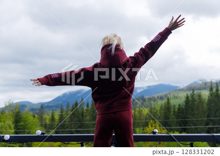Person Enjoying the Great Outdoors Amidst Majestic Mountain Scenery with Arms Outstretched in a Comfortable Hoodie on a Cloudy Day Within Nature's Embrace 128331202