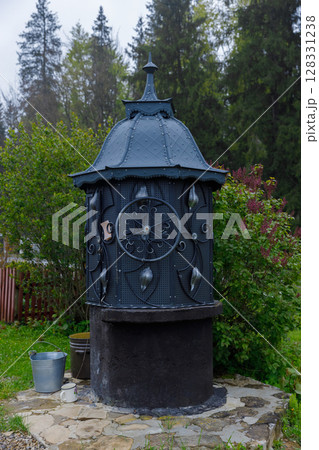 Elegant Ornate Well Surrounded by Lush Greenery, Showcasing the Charm of Rustic Architecture in a Scenic Outdoor Setting 128331238