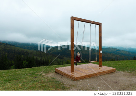 A Serene Wooden Swing Offering Beautiful Mountain Views Surrounded by Clouds and Lush Greenery in a Tranquil Outdoor Setting 128331322