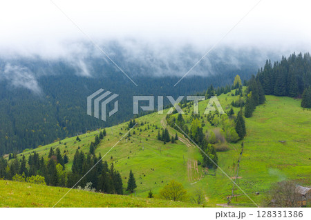 Serene Mountain Landscape with Lush Green Hills and Misty Clouds Above in a Peaceful Natural Setting in Early Spring Serene Mountain Landscape with Lush Green Hills and Misty Clouds Above in a Peaceful Natural Setting in Early Spring 128331386