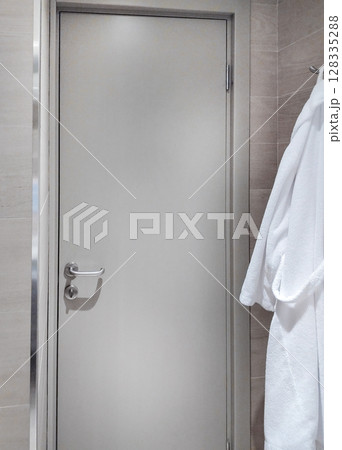 Closed hotel bathroom door, white bathrobes hanging nearby 128335288