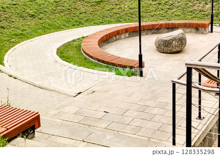 Close-up of a wooden bench and an arc-shaped sidewalk in a city park on a sunny summer day 128335298