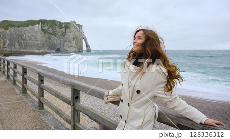 Happy woman enjoying windy day by Etretat cliff in Normandy 128336312