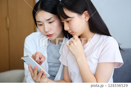 スマホを真剣に見る母と娘のイメージ スマホを真剣に見る母と娘のイメージ 128336529