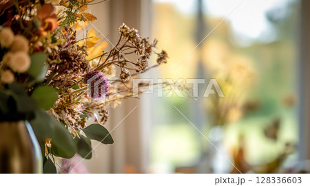 Elegant autumn floral arrangement in warm, muted tones against a bokeh background of golden light. 128336603