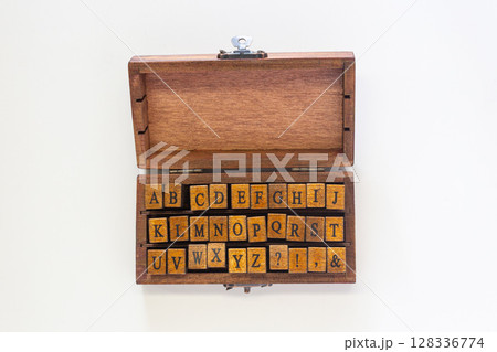 Handcrafted wooden box containing complete alphabet rubber stamps with uppercase letters and punctuation marks, arranged in three neat rows. Perfect for crafting, journaling, and traditional printing  128336774