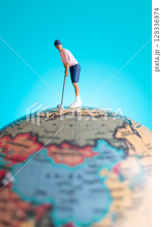 A miniature figure of a golfer playing on top of a globe 128336974
