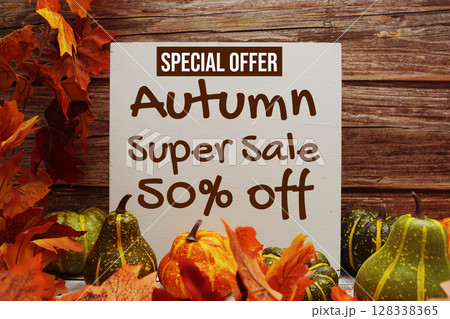 Autumn Super Sale 50% Off Special Offer text with pumkins and maple leaf decoration on wooden background Autumn Super Sale 50% Off Special Offer text with pumkins and maple leaf decoration on wooden background 128338365