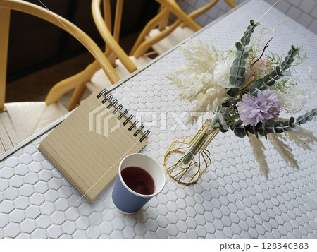 Notebook and tea cup on white tiles table withe stylish gold metal flowers vase 128340383