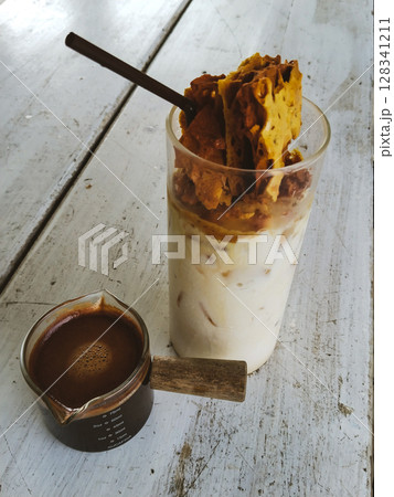 Cold milk with melted toffee sugar in a glass served with strong black coffee on white wooden table 128341211