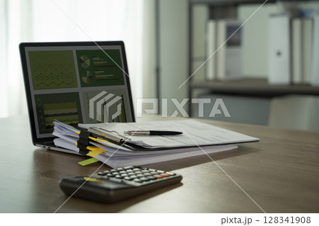 Report file Eco friendly tidy office workspace with documents, pen, calculator, and laptop displaying charts and graphs, suggesting financial 128341908
