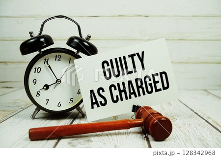 Guilty As Charged text on paper card with alarm clock and wooden judge gavel on wooden background 128342968