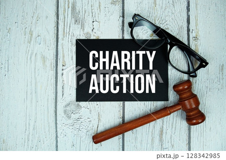 Charity Auction text on paper card with alarm clock and wooden judge gavel top view on wooden background 128342985