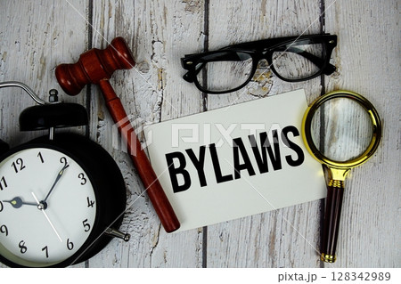 Bylaws text on paper card with alarm clock and wooden judge gavel top view on wooden background Bylaws text on paper card with alarm clock and wooden judge gavel top view on wooden background 128342989