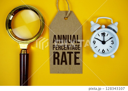Annual Percentage Rate text on price tag with magnifying glass and alarm clock on yellow background Annual Percentage Rate text on price tag with magnifying glass and alarm clock on yellow background 128343107