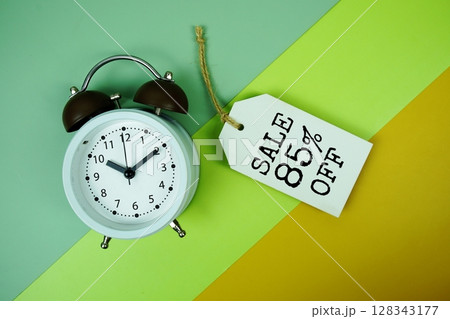 Sale 85% off text on price tag with alarm clock on green, yellow geometric background 128343177