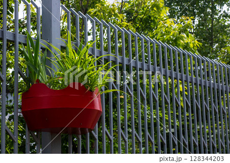 A red planter with various plants hangs from a sturdy metal fence A red planter with various plants hangs from a sturdy metal fence 128344203