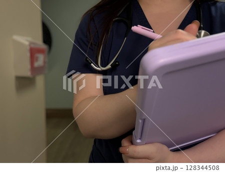 Nurse Writing on Clipboard in Hallway with Stethoscope Around Neck 128344508